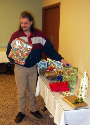Terry holding a wrapped present standing in front of a table full of presents